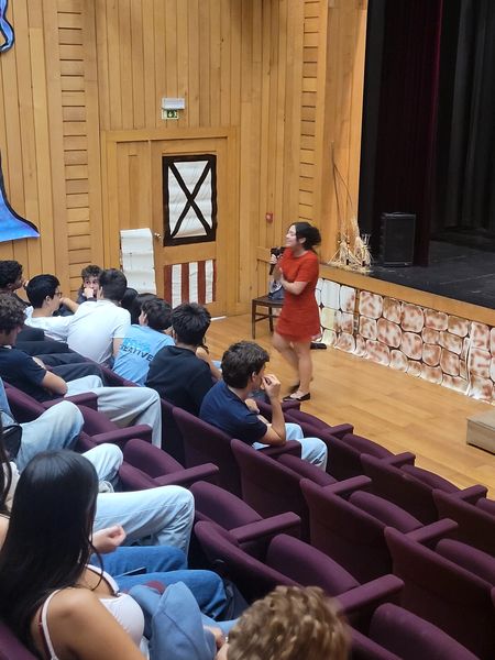 Mulher de vestido vermelho caminha em frente às filas de estudantes enquanto fala